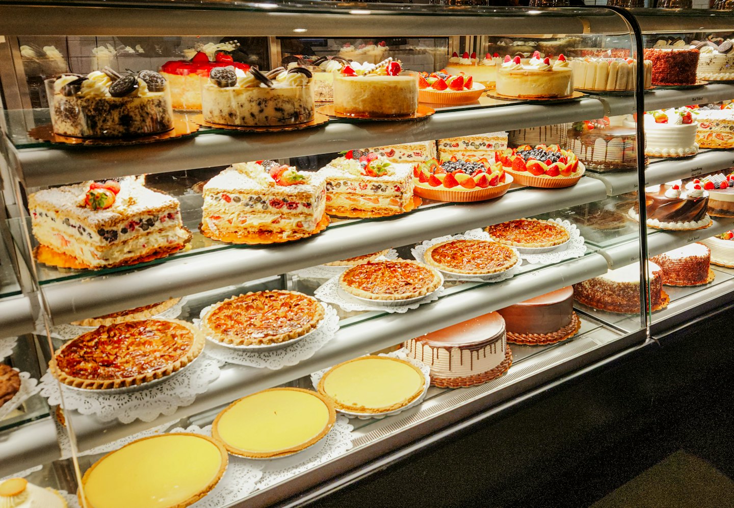 Bakery display case filled with assorted cakes and fruit tarts.