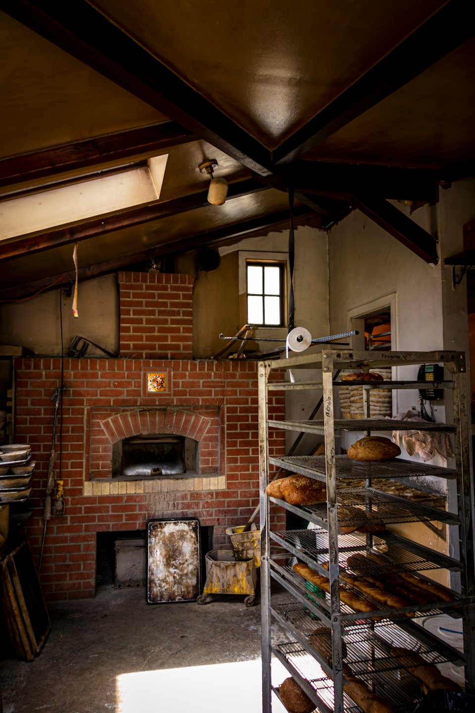 Freshly baked bread sits on shelves near a rustic brick oven.