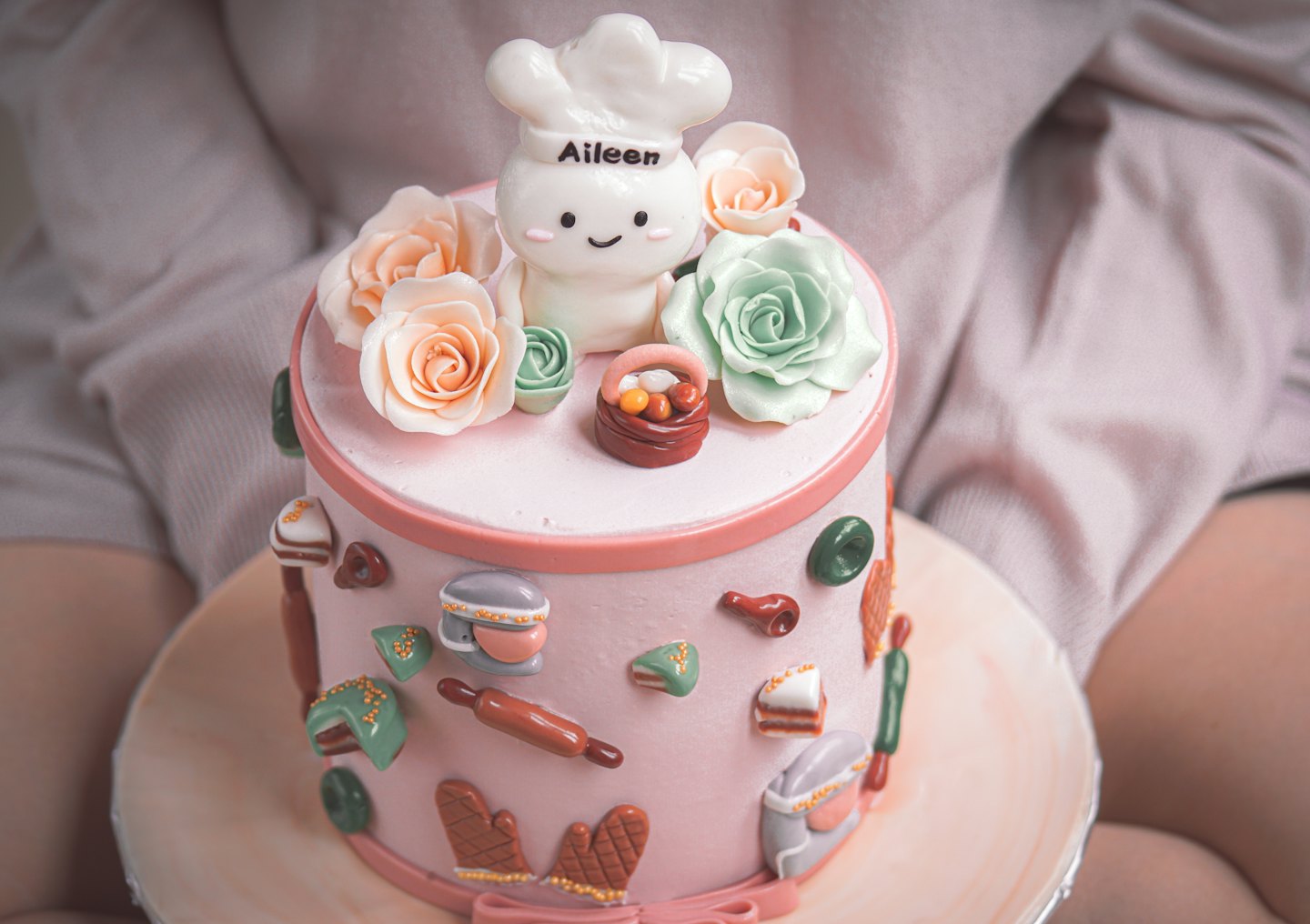 A person holds a pink cake decorated with fondant baking tools.