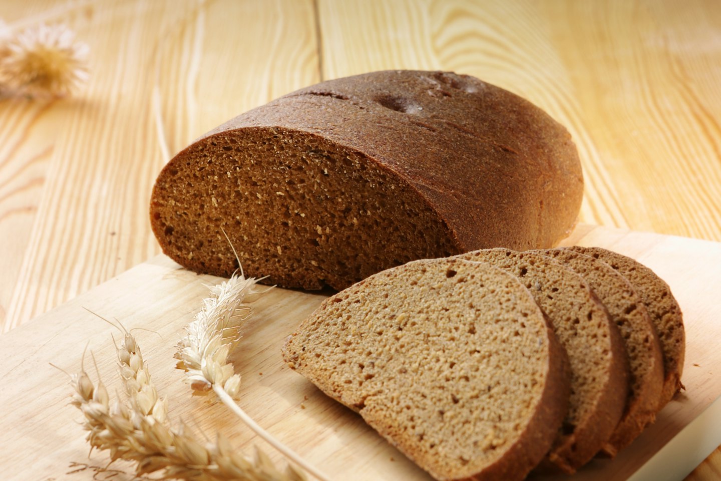 Sliced rye bread and wheat stalks on a wooden board.