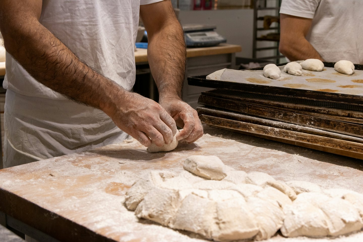 Baker shapes dough portions on a wooden workbench.
